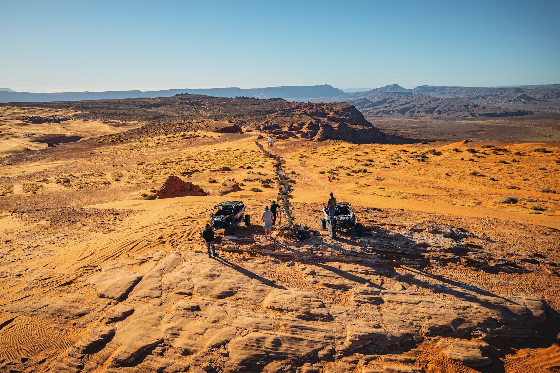 Riders pause at the peak of a scenic desert trail with UTVs in Southern Utah, showcasing expansive sand dunes and rugged terrain.