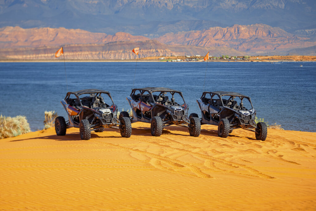 Three UTVs parked on Sand Hollow’s orange dunes with a lake backdrop, showcasing Southern Utah’s UTV rental adventure.