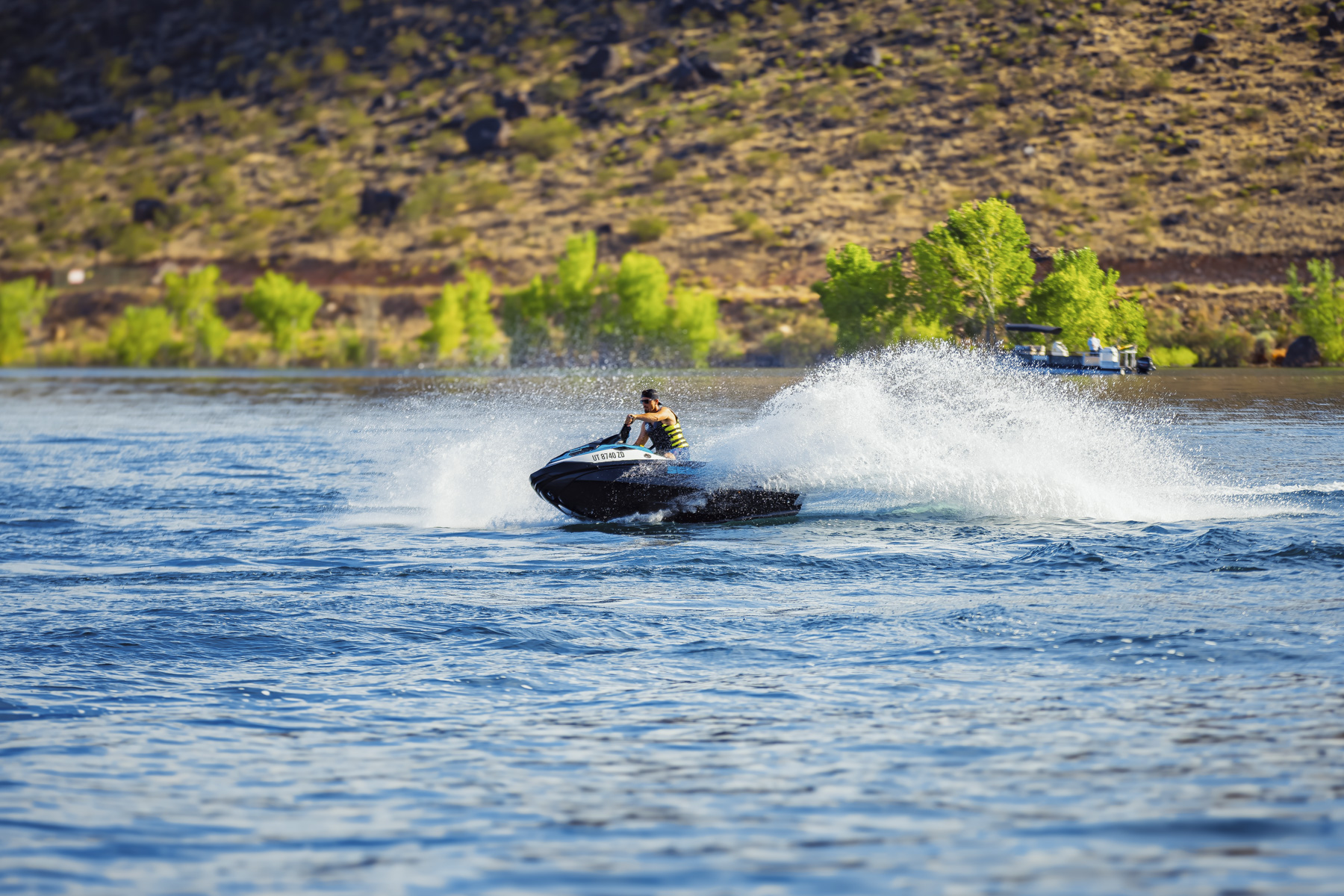 Man riding jet ski across Quail Creek Reservoir in southern Utah with water spray and shoreline trees in the background