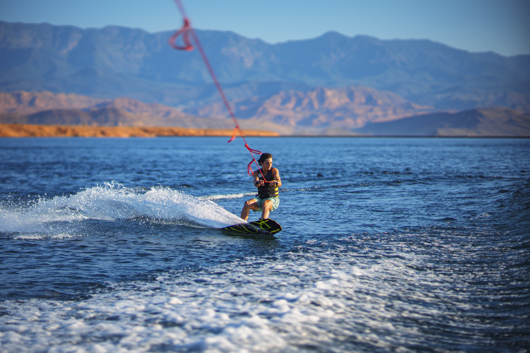 Wakeboarder carves across Sand Hollow Lake under blue skies during a Southern Utah adventure water sports experience.